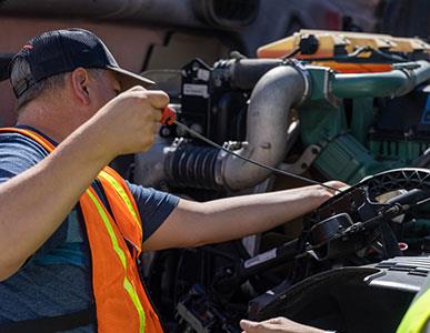 man in orange safety vest checking the oil of a vehicle