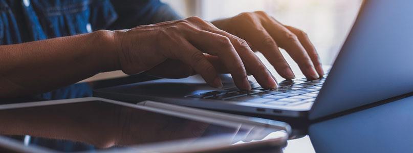 a person's hands resting on the keyboard of an open laptop on a desk