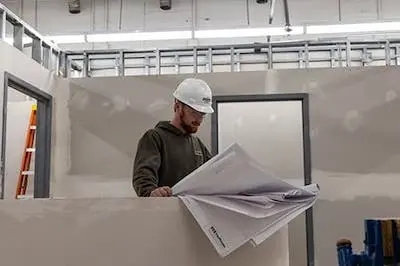 construction worker looking at design plans inside building under construction