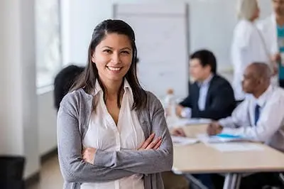 person standing with arms folded in a meeting room smiling at the camera