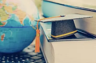 small paper graduation cap sitting on books next to plastic globe