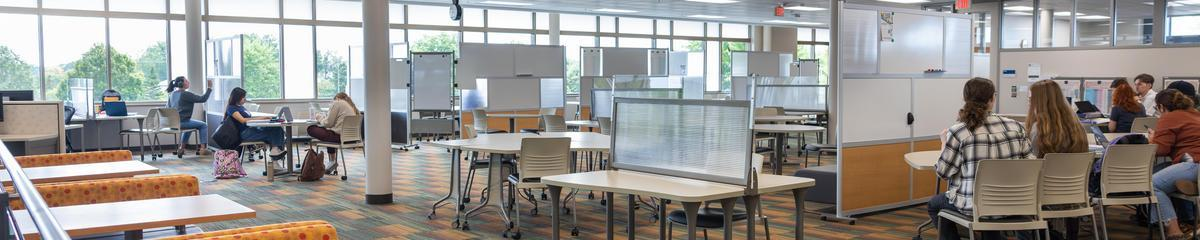 Three students studying at a table with students walking down the hall